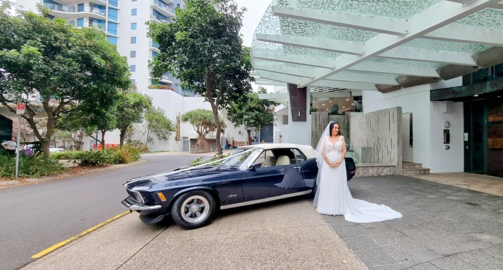 Bride standing with dark blue Ford Mustang wedding car rental