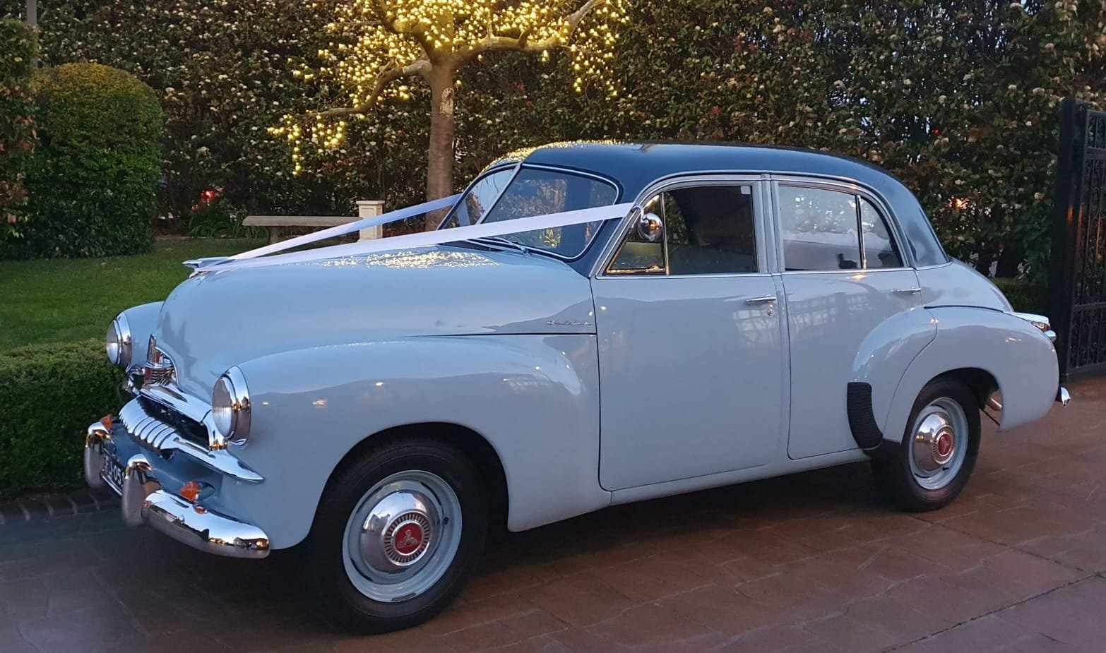 Vintage light blue 1955 FJ Holden Special wedding hire car parked on a residential driveway.