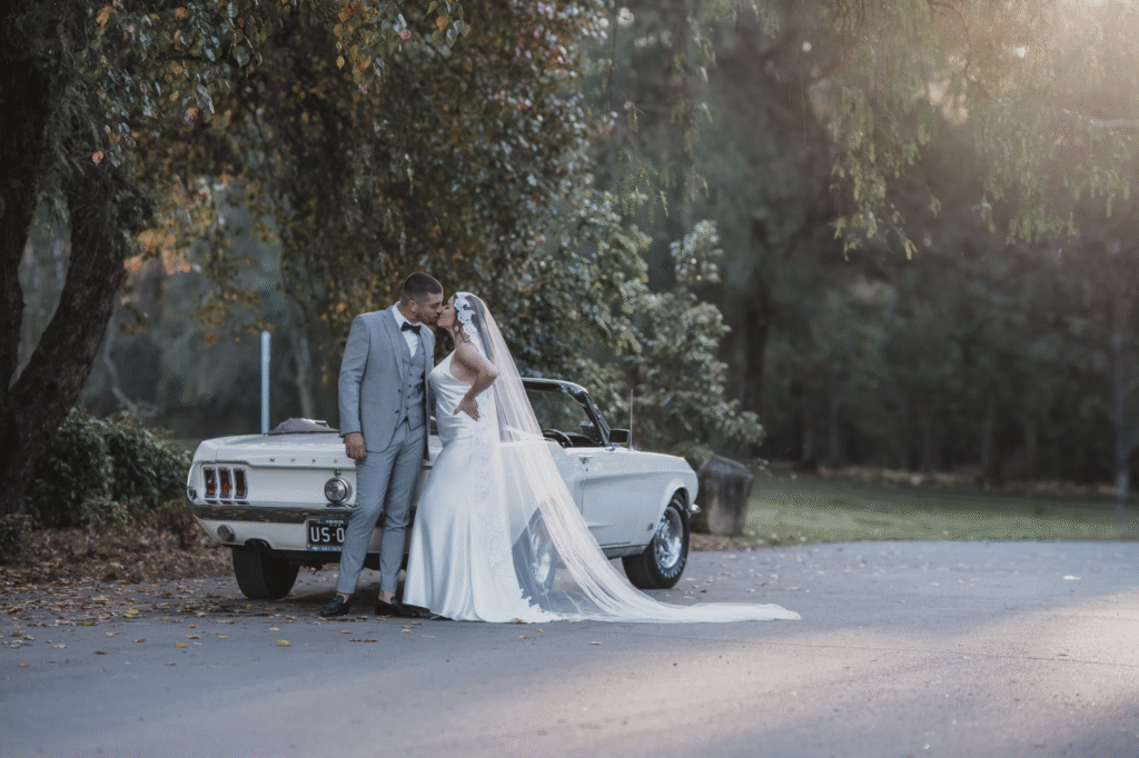 Bride and groom posing next to a classic white car for wedding car hire Sydney