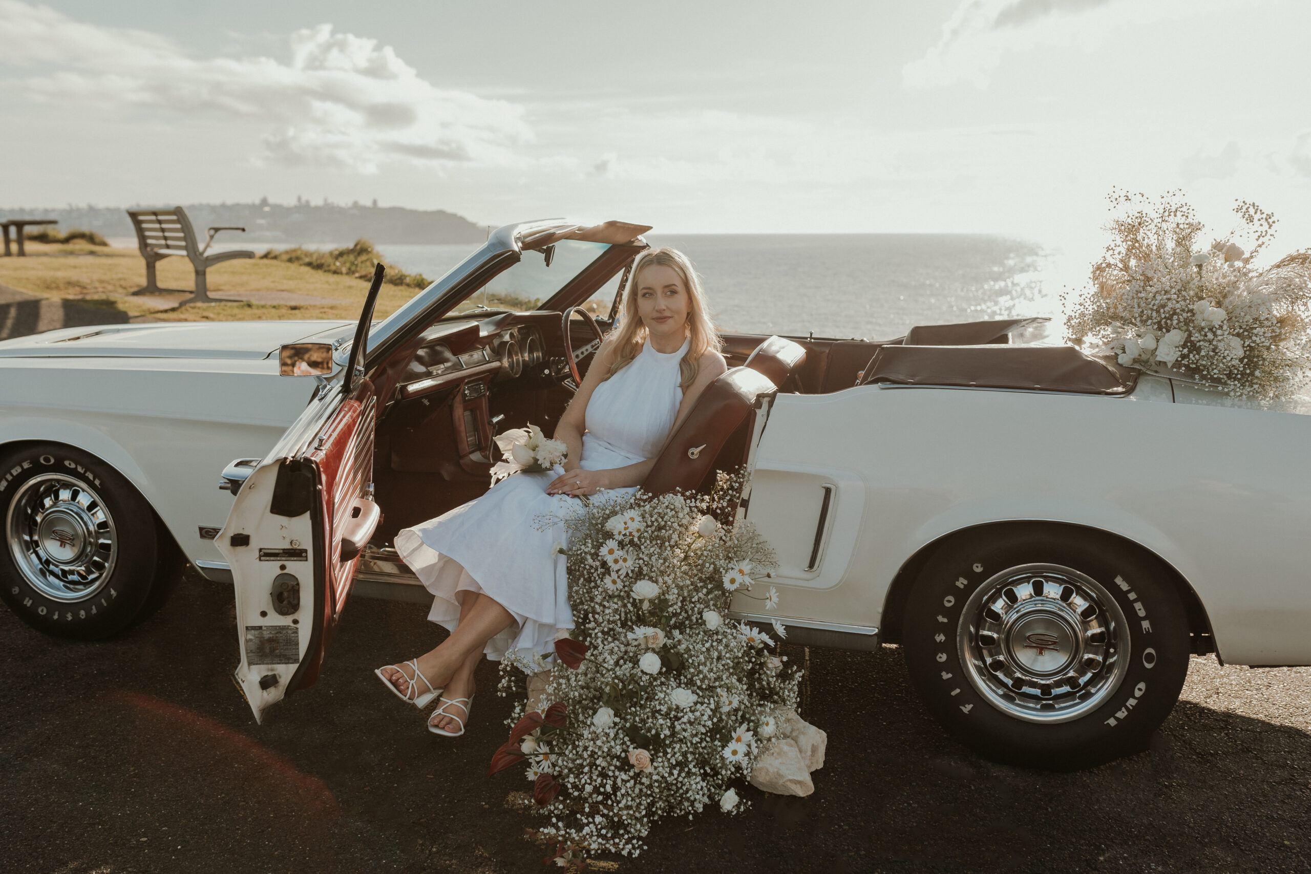 Bride and groom posing with a vintage Wimbledon White Ford Mustang convertible wedding car in Sydney.