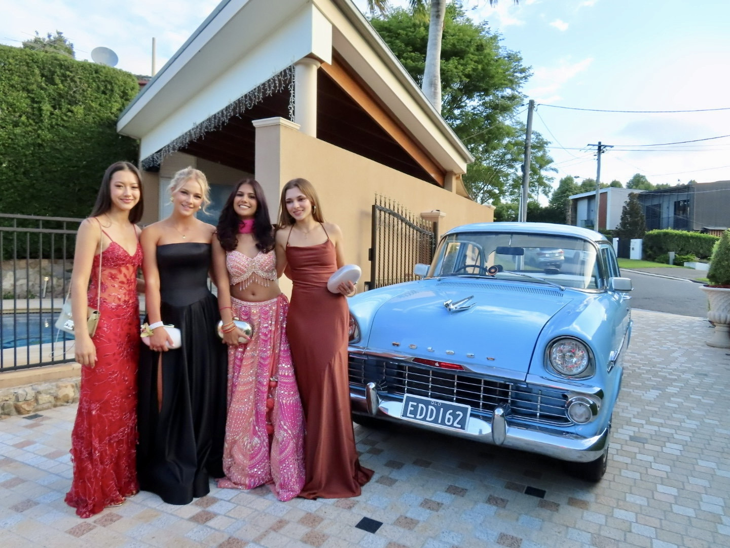 Students posing in formal gowns beside 1962 Holden EK Eddie the EK school formal car hire Brisbane